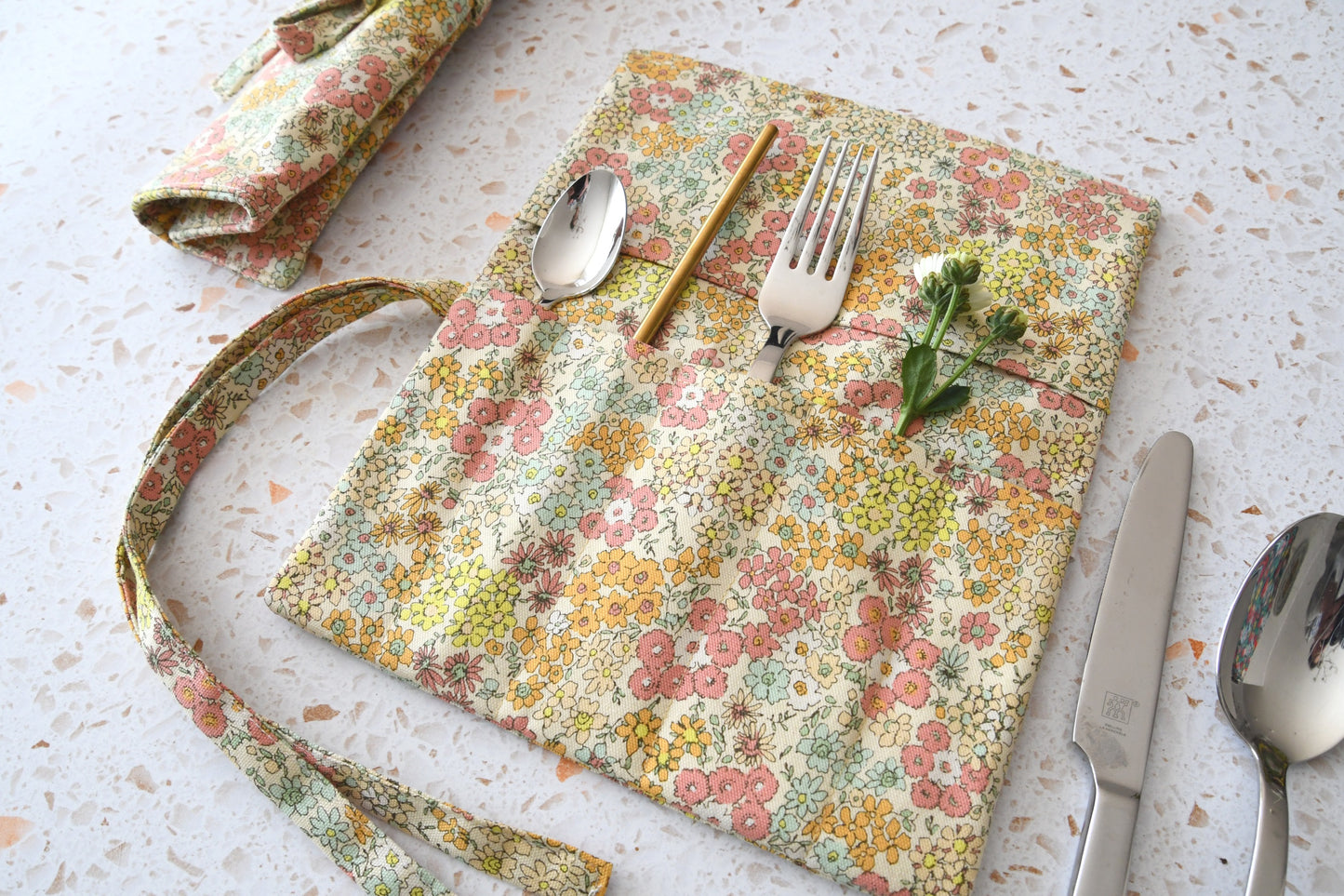 Handgenähte Besteckrolle aus Stoff mit romantischem Blumenmuster, geöffnet und mit Besteck bestückt.
