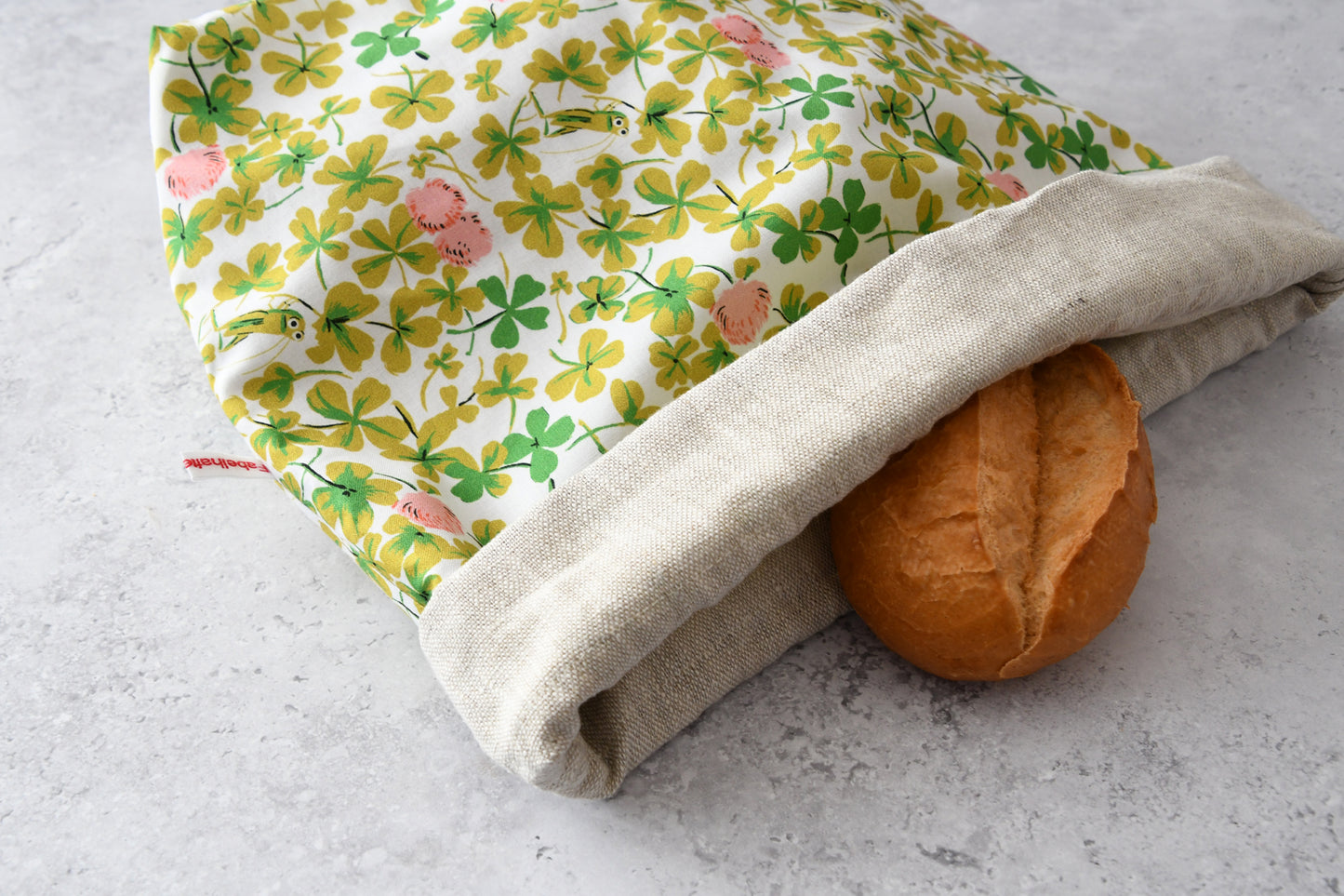 Liegender Brotbeutel "Grashüpfer im Klee" aus Baumwolle, bei dem das atmungsaktive Innenfutter aus 100% Leinen gut zu sehen ist, von Fabelhaftewerkstatt.