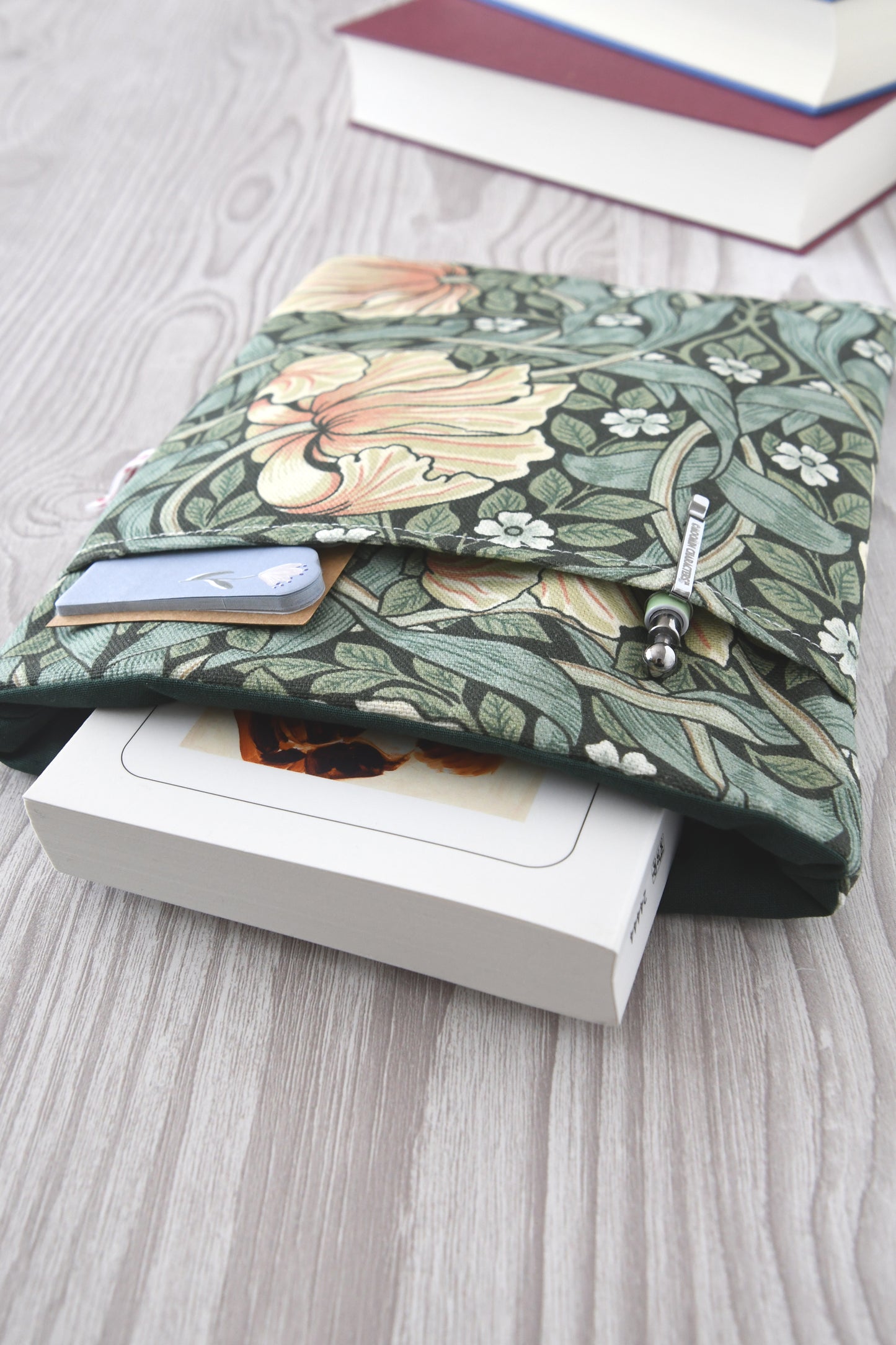 Draufsicht auf die geöffnete Buchtasche im William Morris Stil mit eingestecktem Buch sowie einem Stift und Lesezeichen in der Vordertasche.