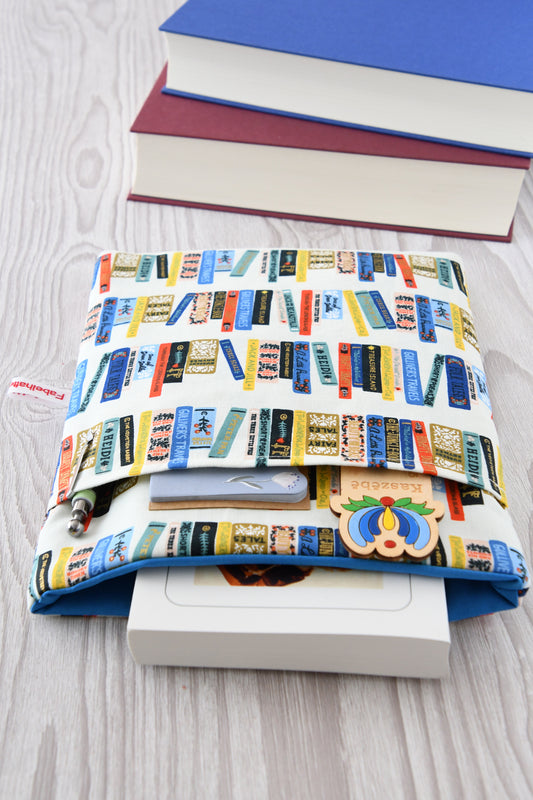 Detailreiches Foto einer Buchtasche mit Bücherrücken-Print. Aus der weichen Hülle schaut ein echtes Buch heraus. Das clevere Zubehörfach auf der Vorderseite ist mit Zubehör bestückt, um den perfekten Schutz für unterwegs zu demonstrieren.