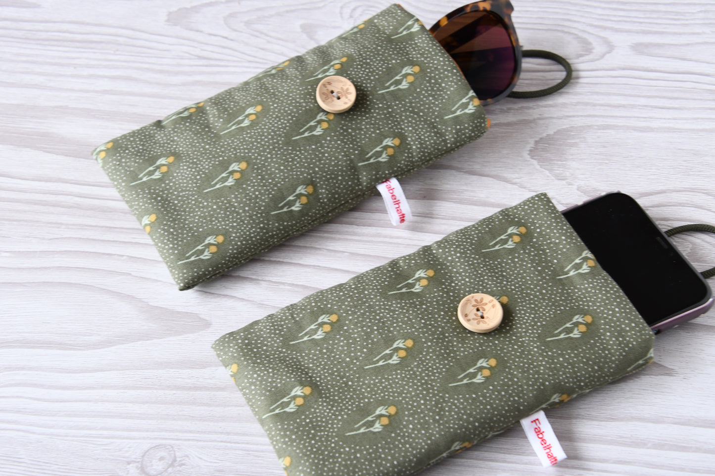 Zwei handgenähte Stofftaschen von Fabelhafte Werkstatt nebeneinander: Eine genutzt als schützende Handyhülle mit Smartphone, die andere als leichtes Brillenetui mit einer Sonnenbrille.