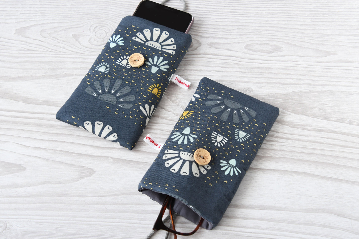 Zwei handgenähte Stofftaschen von Fabelhafte Werkstatt nebeneinander: Eine genutzt als schützende Handyhülle mit Smartphone, die andere als leichtes Brillenetui mit einer Brille.