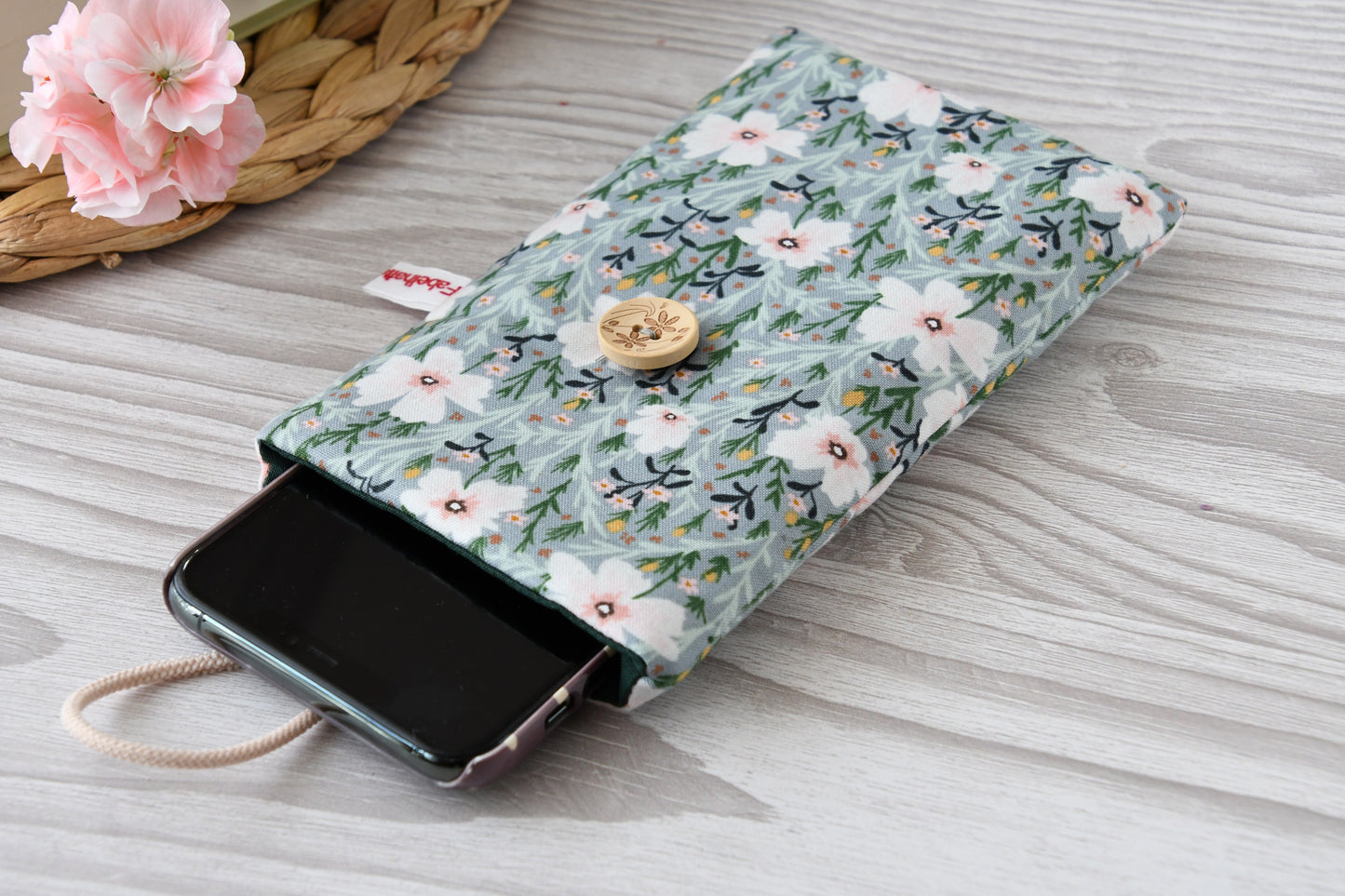 Geöffnete Stoff-Handyhülle mit Blumenmuster und einem Smartphone, das darin sicher vor Kratzern geschützt wird.