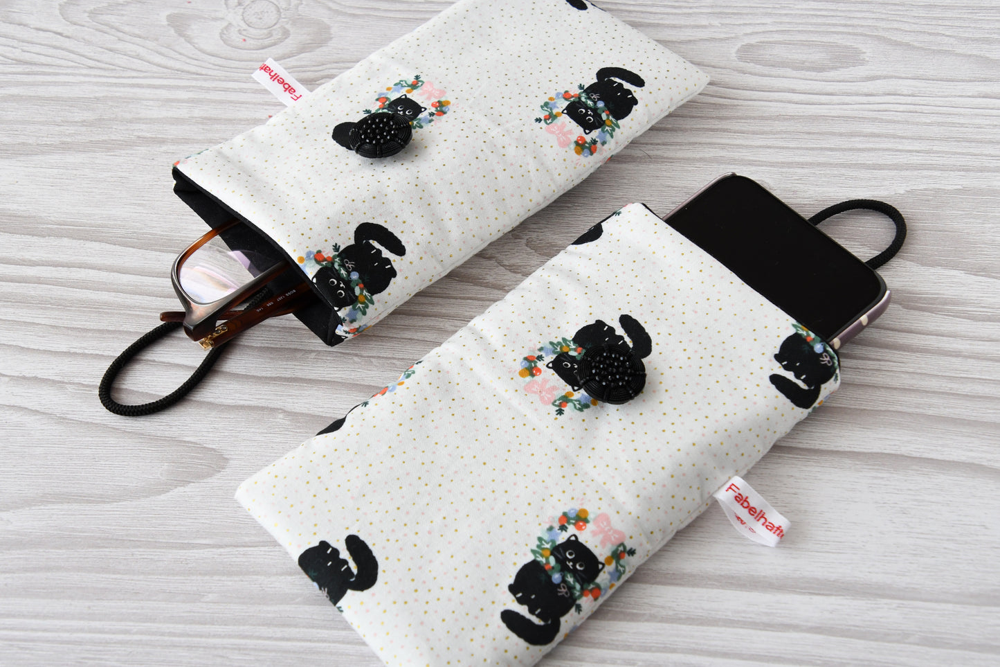 Zwei handgenähte Stofftaschen von Fabelhafte Werkstatt nebeneinander: Eine genutzt als schützende Handyhülle mit Smartphone, die andere als leichtes Brillenetui mit einer Sonnenbrille.