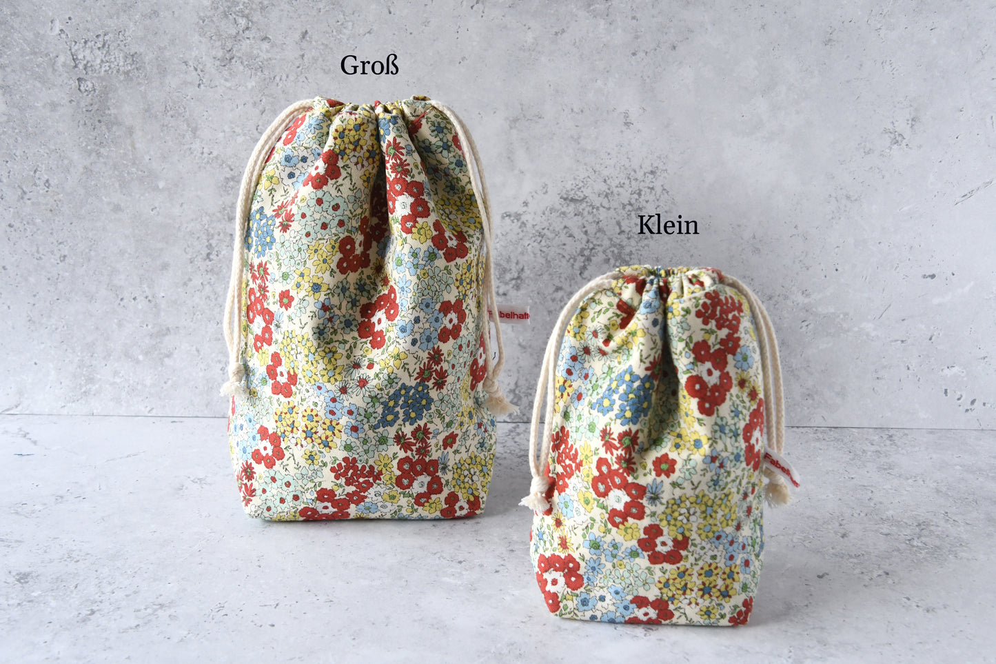 Größenvergleich der handgemachten Kinchaku-Beutel mit rotfarbenem Streublumen-Muster von Fabelhafte Werkstatt: Das kleine und große Modell nebeneinander.