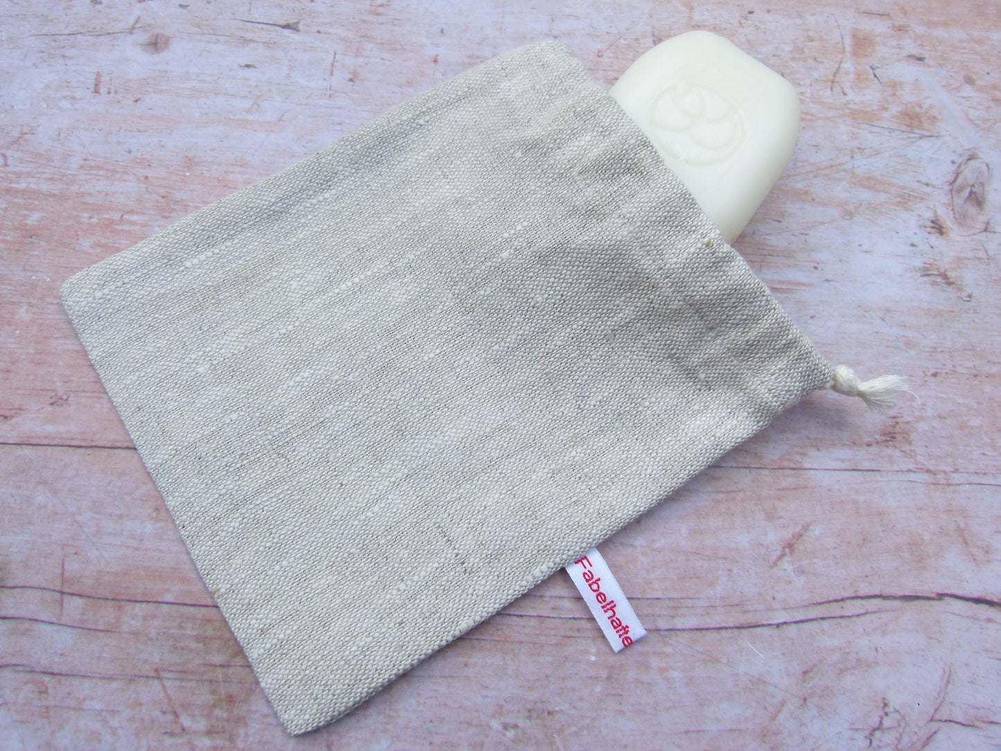 Handgenähtes Seifensäckchen von Fabelhaftewerkstatt aus reinem Leinen in der Farbe Natur, aus dem ein Stück feste Duschseife herausschaut.