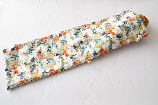 Ein handgenähter, langer Baguettebeutel aus  liegt auf einer hellen Küchenarbeitsplatte. Ein frisches, knuspriges Baguette schaut oben leicht aus der geöffneten Kordelöffnung heraus.