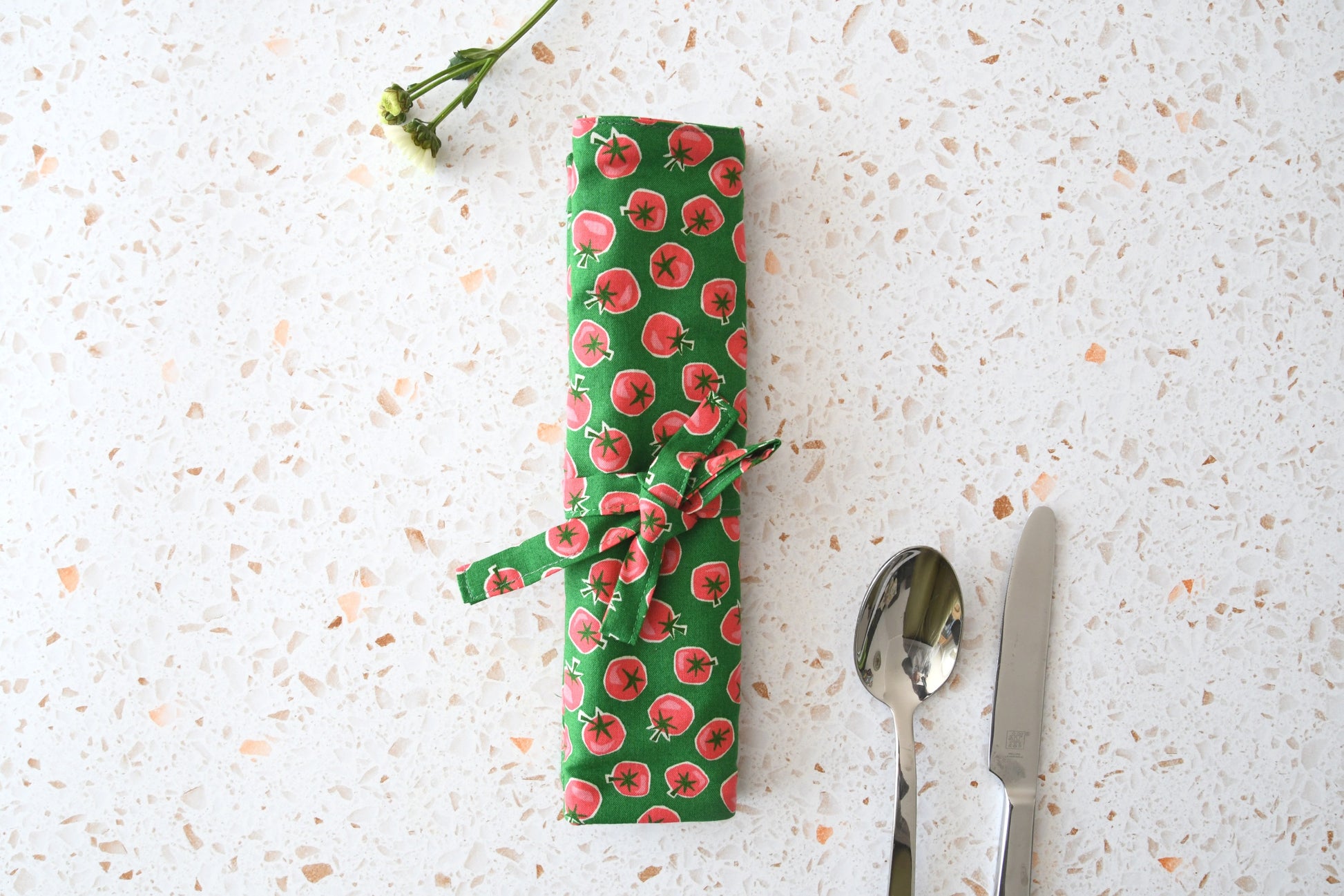Kompakt eingerollte Bestecktasche für unterwegs mit rotem Tomatenmuster auf hellem Stoff.