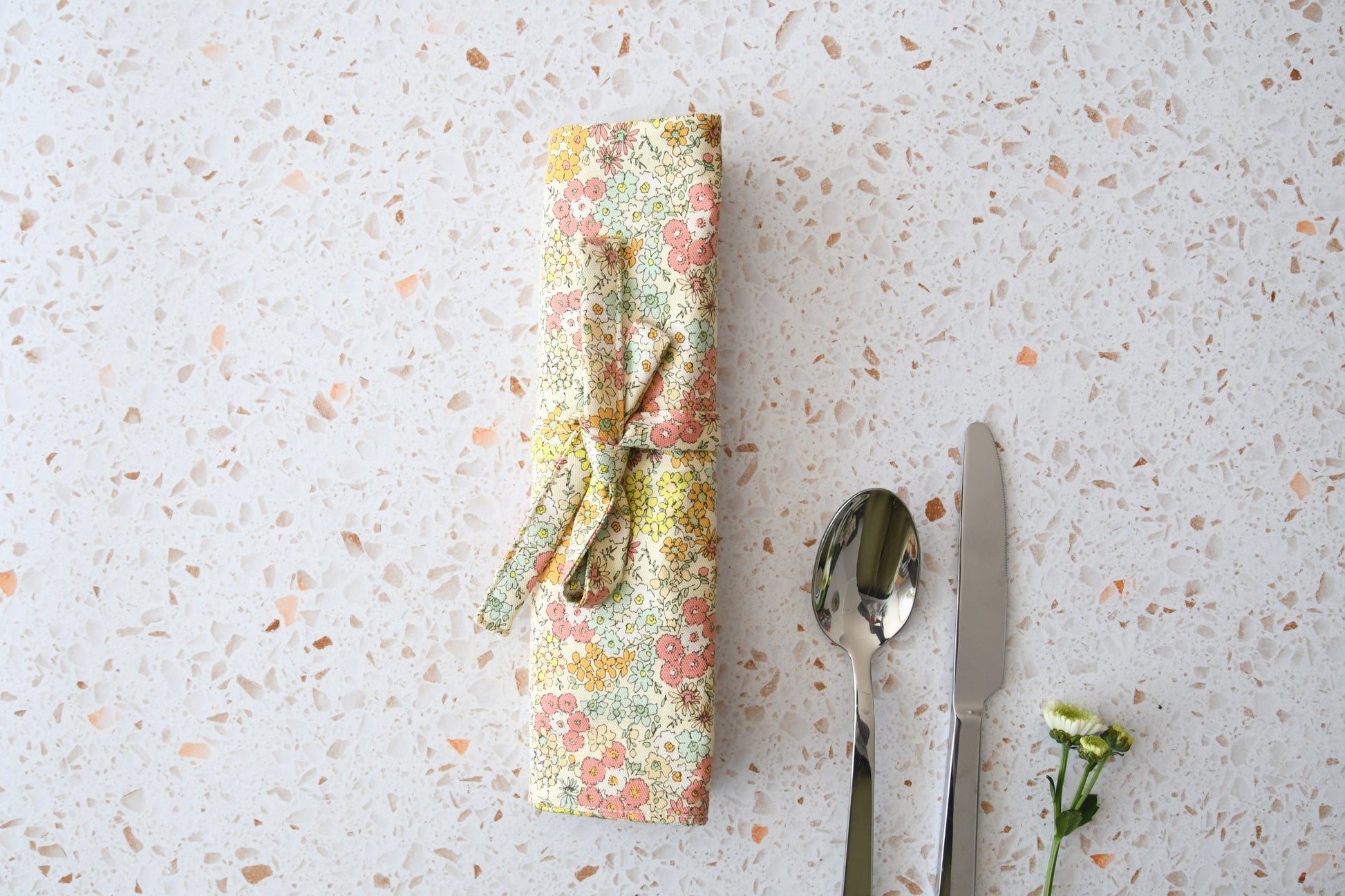 Kompakt zusammengerollte Bestecktasche mit Blumenmuster, verschlossen mit einem passenden Stoffband.