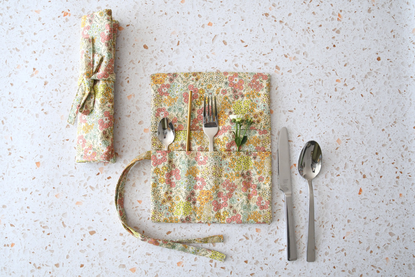 Handgenähte Besteckrolle aus Stoff mit romantischem Blumenmuster, geöffnet und mit Besteck in den Fächern bestückt.