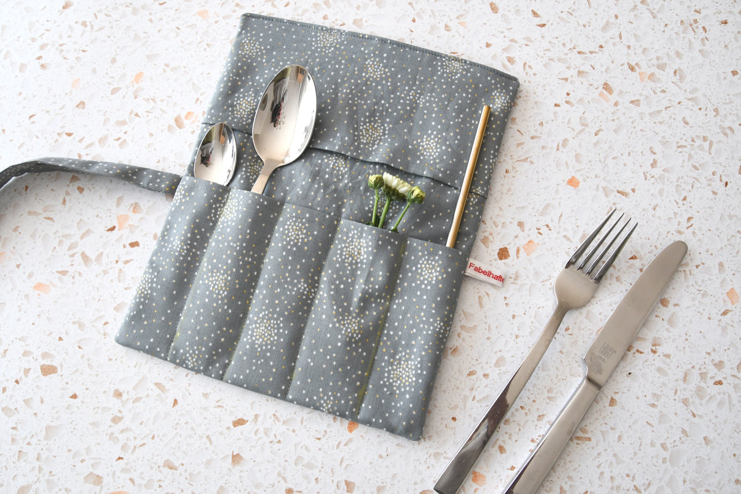 Elegante Besteckrolle aus grauem Stoff mit funkelndem Glitter-Effekt, geöffnet und mit Besteck für die Mittagspause bestückt.