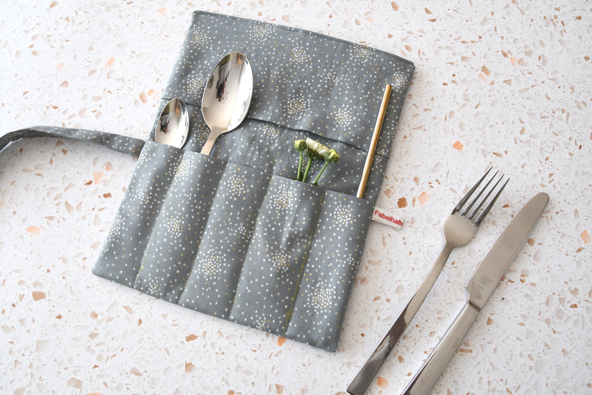 Elegante Besteckrolle aus grauem Stoff mit funkelndem Glitter-Effekt, geöffnet und mit Besteck für die Mittagspause bestückt.