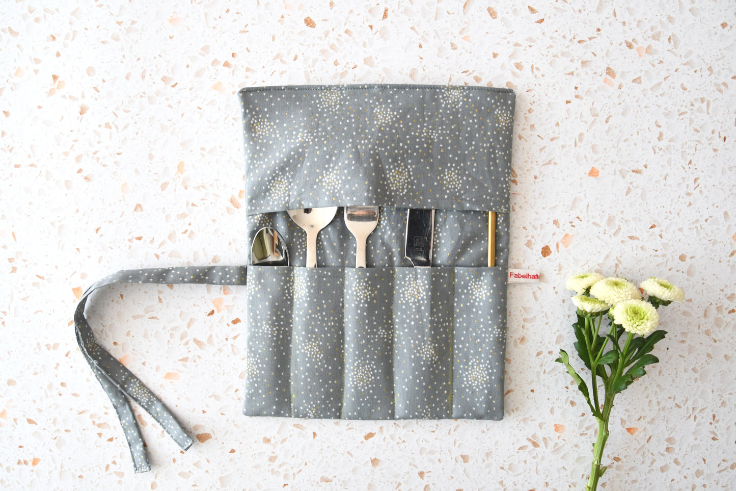 Elegante Besteckrolle aus grauem Stoff mit funkelndem Glitter-Effekt, geöffnet und mit Besteck bestückt.