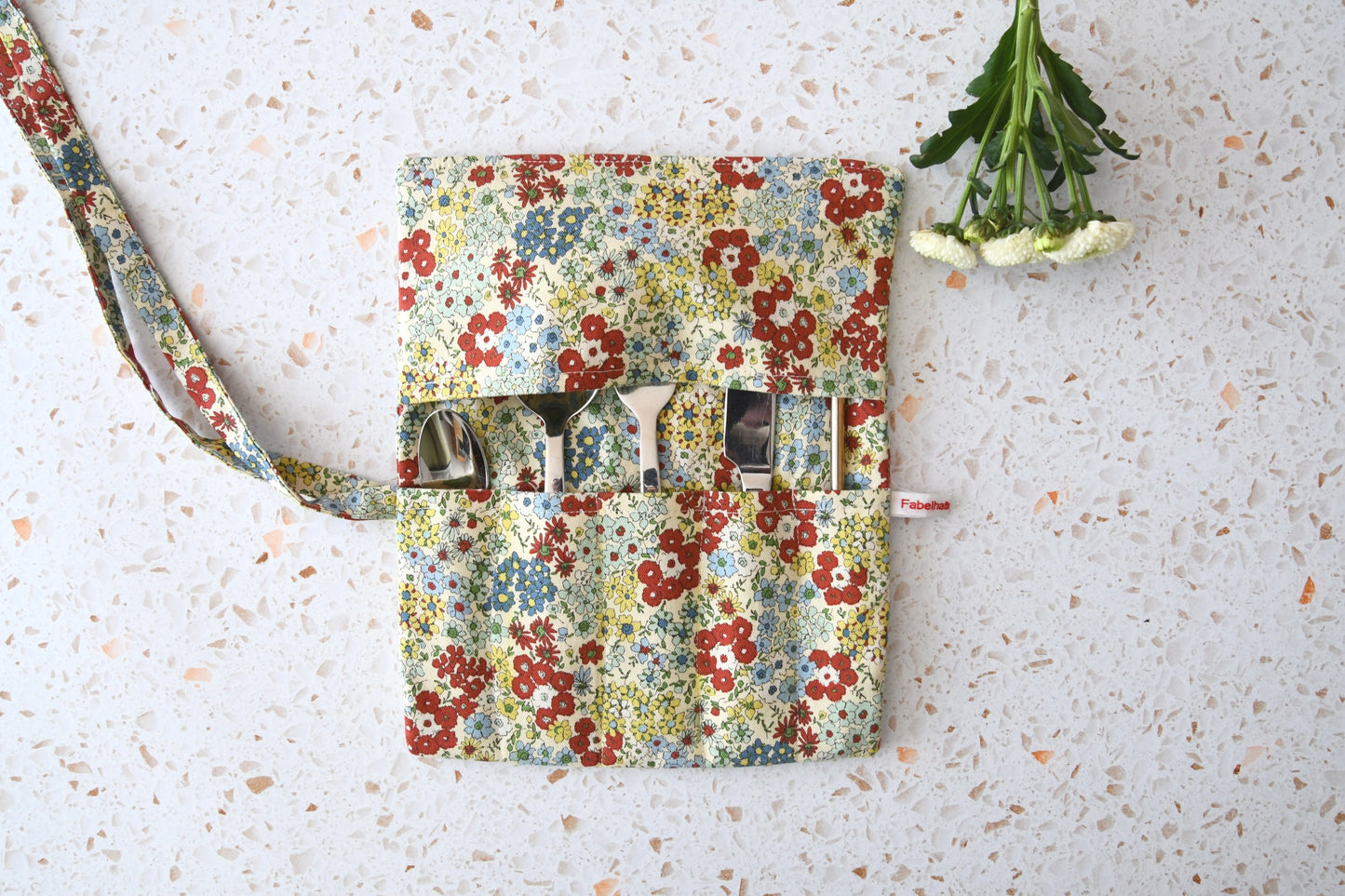 Handgenähte Besteckrolle aus Stoff mit romantischem Blumenmuster, geöffnet und mit Messer, Gabel und Löffel in den Fächern bestückt.