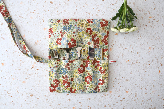 Handgenähte Besteckrolle aus Stoff mit romantischem Blumenmuster, geöffnet und mit Messer, Gabel und Löffel in den Fächern bestückt.