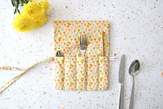 Handgenähte Besteckrolle aus Stoff mit sommerlichem Blumenmuster, geöffnet und mit Messer, Gabel und Löffel in den Fächern bestückt.