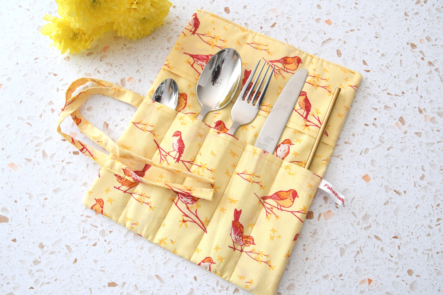 Farbenfrohe Besteckrolle aus gelbem Baumwollstoff mit Vögeln, geöffnet mit eingelegtem Besteck.