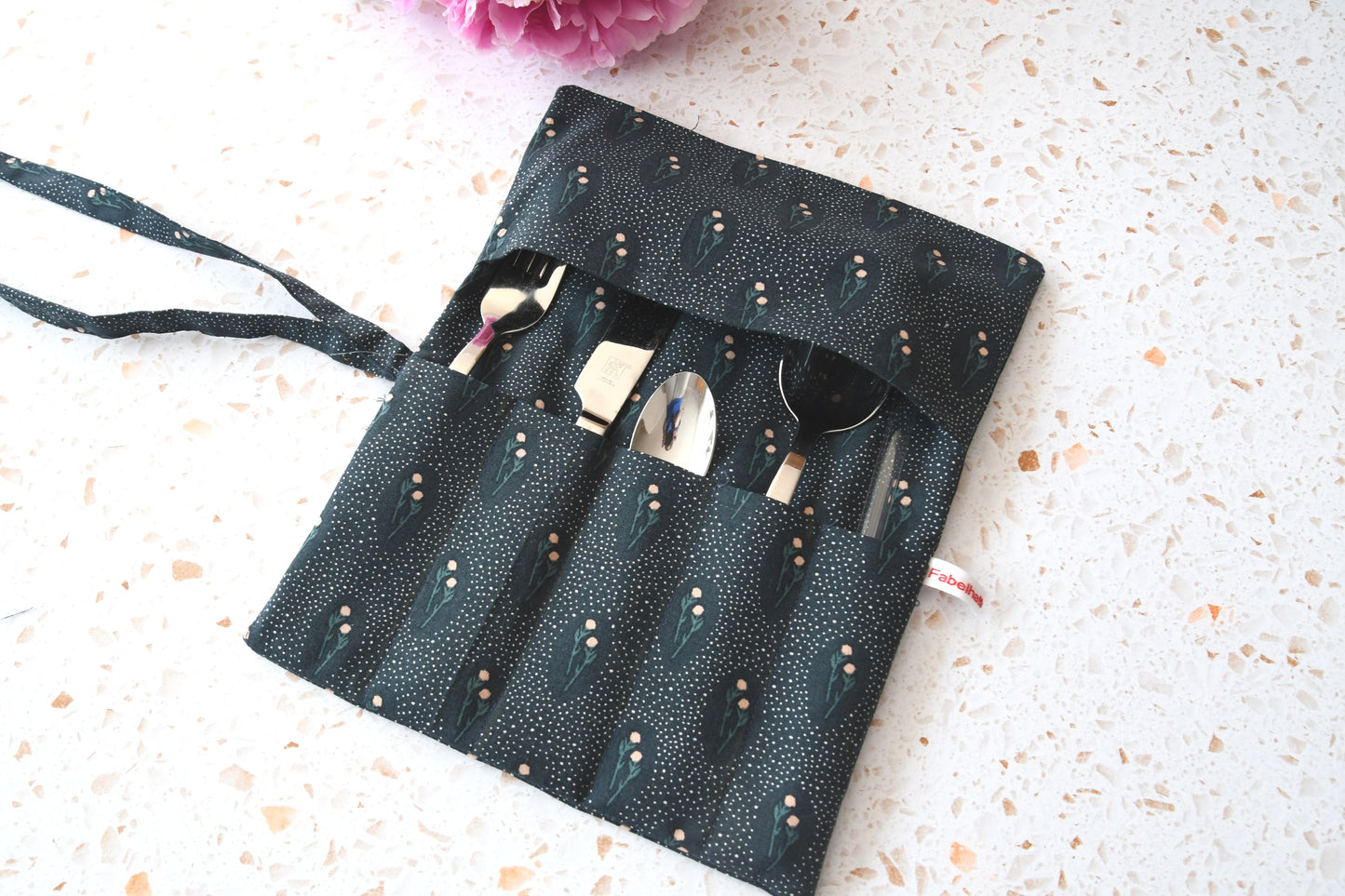 Handgenähte Besteckrolle aus Stoff mit Blumenmuster, geöffnet und mit Messer, Gabel und Löffel in den Fächern bestückt.