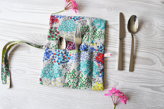 Handgenähte Besteckrolle aus Stoff mit buntem Blumenmuster, geöffnet und mit Messer, Gabel und Löffel in den Fächern bestückt.