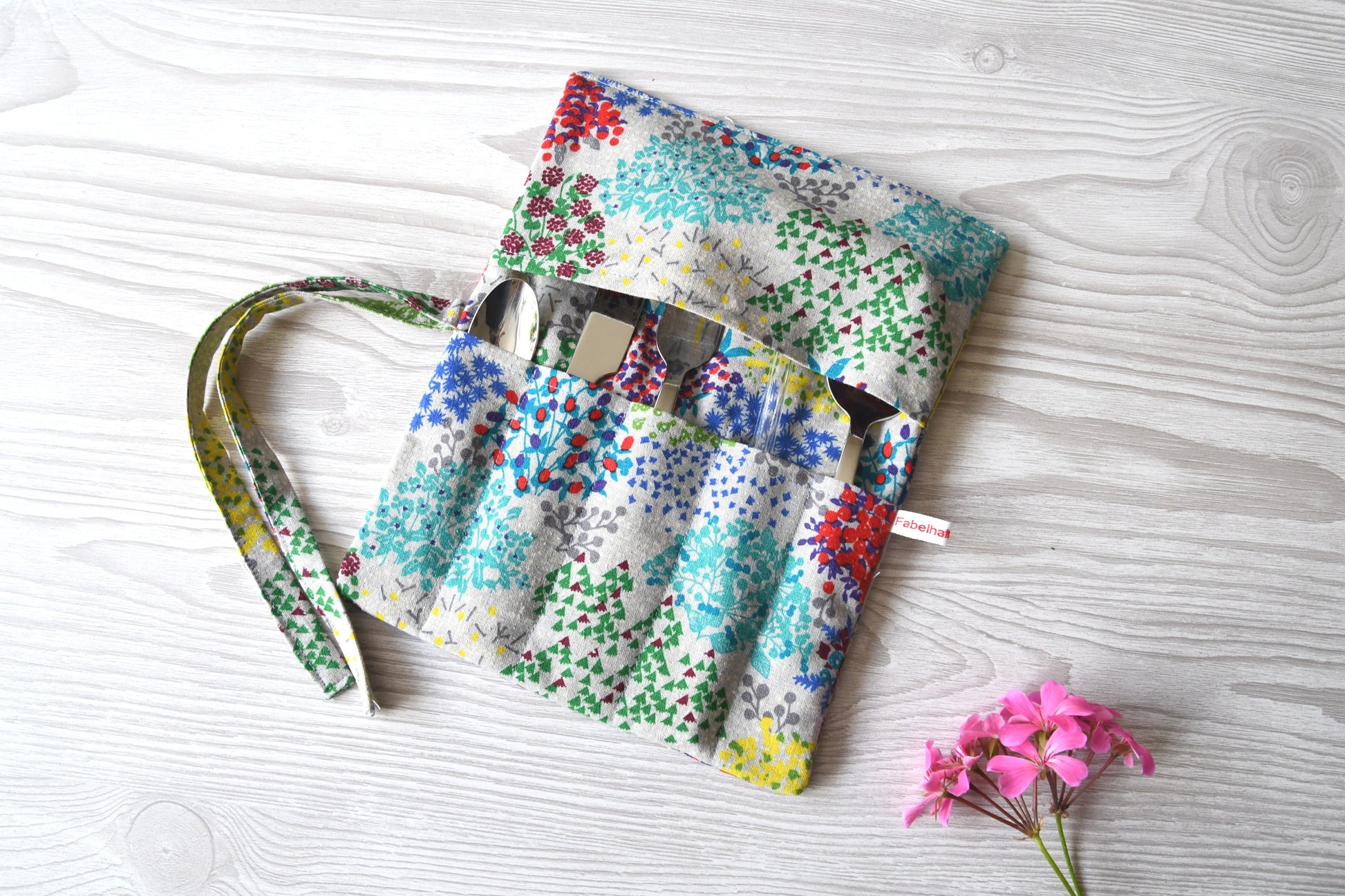 Handgenähte Besteckrolle aus Stoff mit Blumenmuster, geöffnet und mit Messer, Gabel und Löffel in den Fächern bestückt.