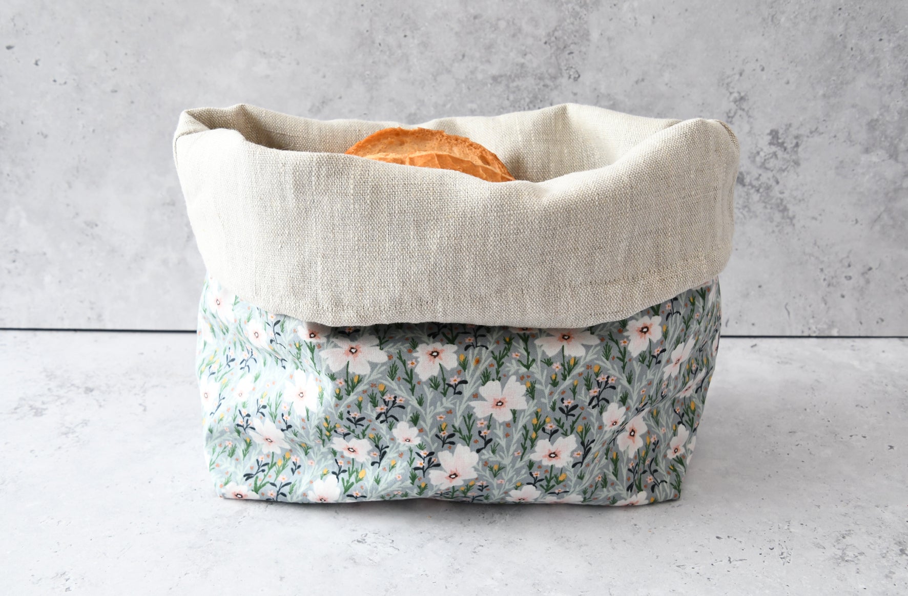 Brotbeutel "Hanna" mit Blumenmuster von Fabelhaftewerkstatt aus Baumwolle, der umgeklappt als Brotkorb mit frischen Brötchen steht.