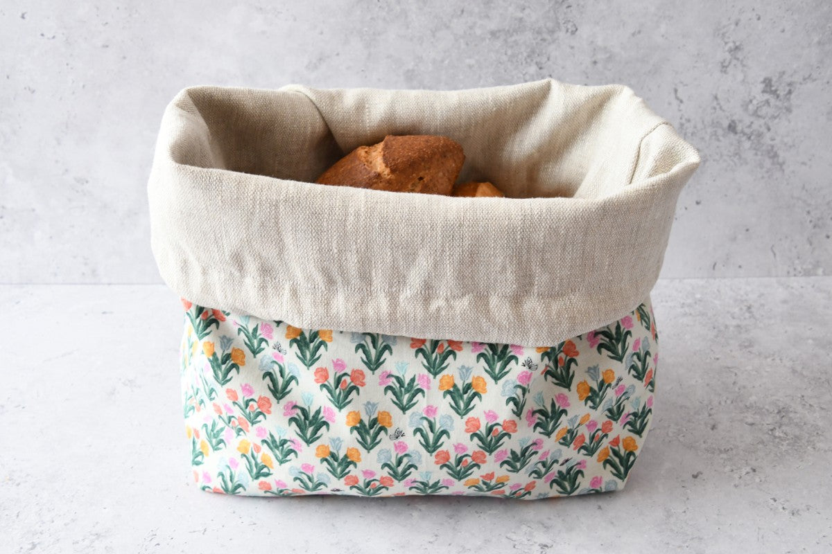 Brotbeutel "Kleine Tulpen" von Fabelhaftewerkstatt aus Baumwolle und Leinen der umgeklappt als Brotkorb mit frischen Brötchen steht.