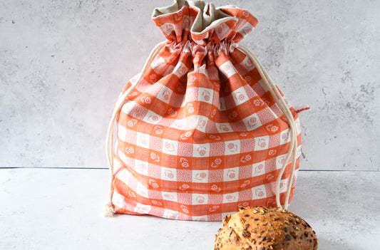 Wiederverwendbarer Brotbeutel Carola orange aus Baumwolle mit orangem Karomuster und Blumen, geschlossen für die frische Aufbewahrung von Brot und Brötchen.