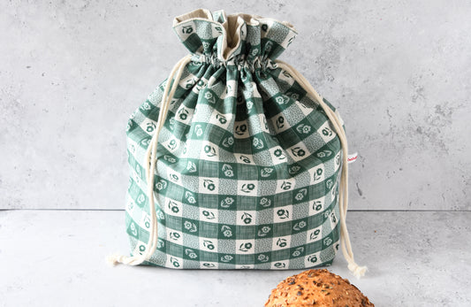 Wiederverwendbarer Brotbeutel Carola grün aus Baumwolle mit grünem Karomuster und Blumen, geschlossen für die frische Aufbewahrung von Brot und Brötchen.