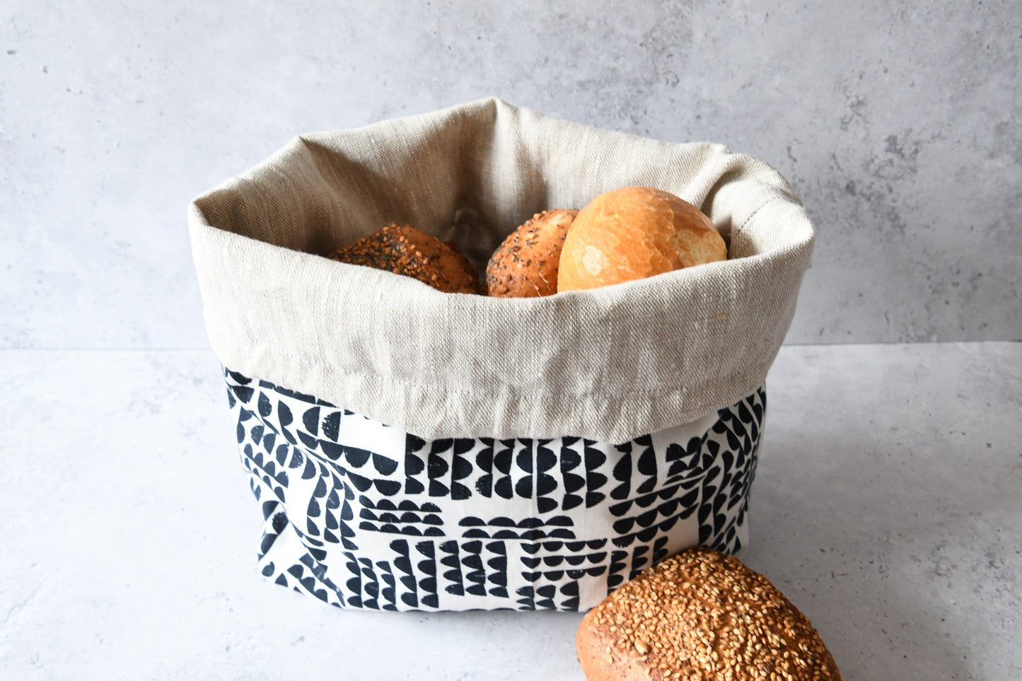 Brotbeutel "Lea" von Fabelhaftewerkstatt aus Baumwolle und Leinen, der umgeklappt als Brotkorb mit frischen Brötchen steht.