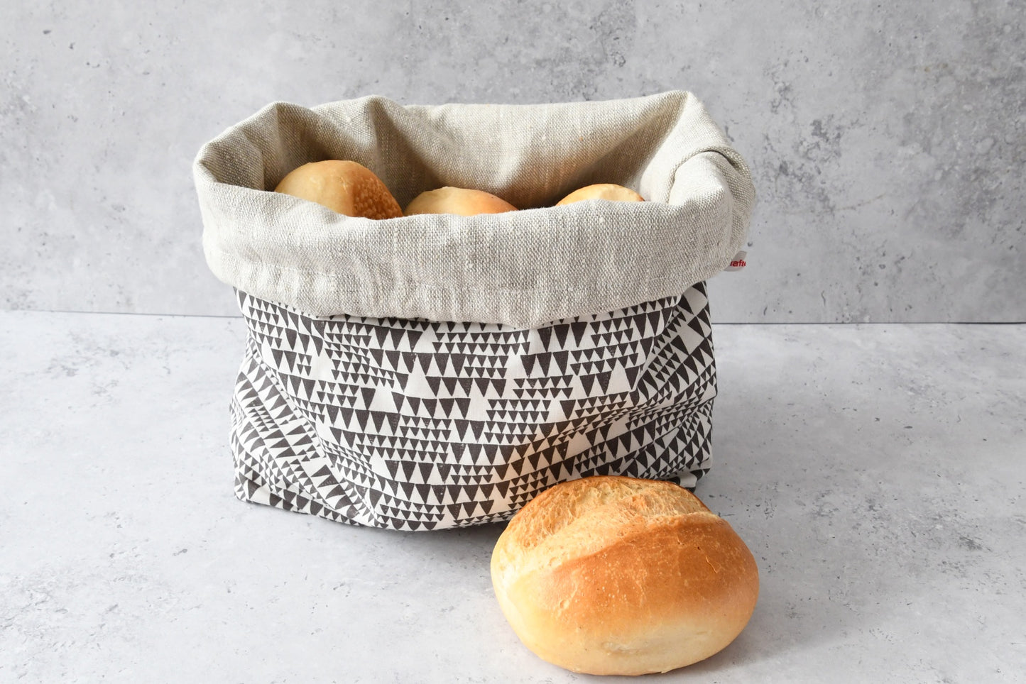 Brotbeutel "Mia" von Fabelhaftewerkstatt aus Baumwolle und Leinen, der umgeklappt als Brotkorb mit frischen Brötchen steht.