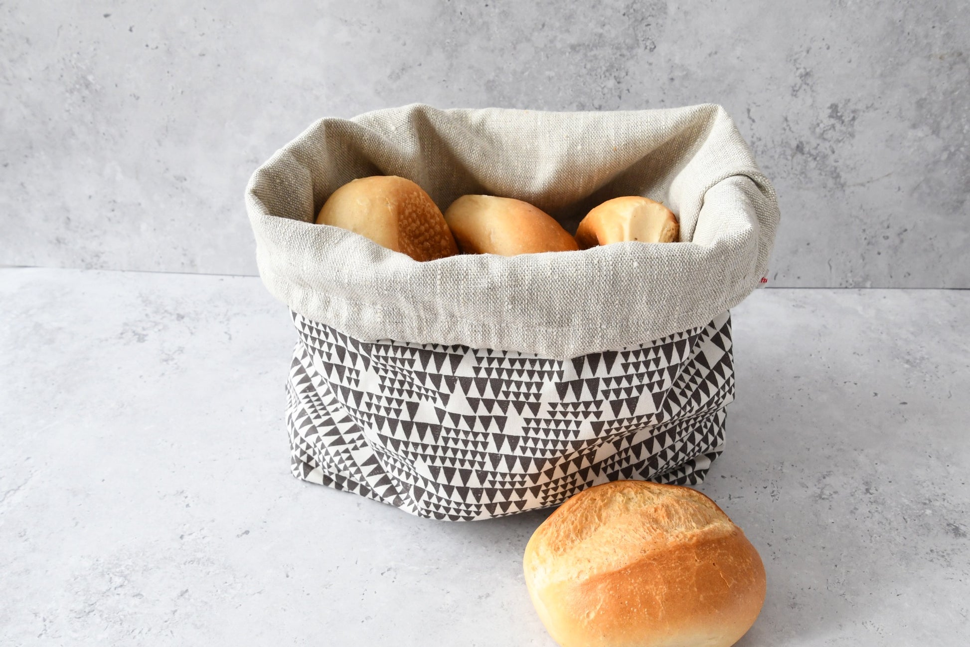Brotbeutel "Mia" von Fabelhaftewerkstatt aus Baumwolle und Leinen, der umgeklappt als Brotkorb mit frischen Brötchen steht.