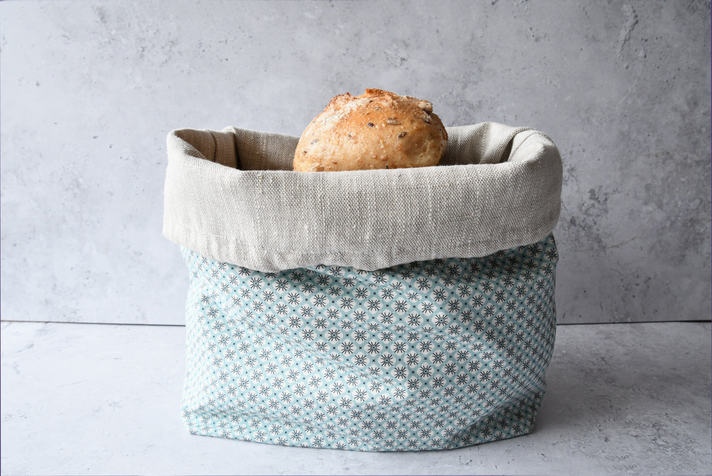 Brotbeutel "Primel" von Fabelhaftewerkstatt aus Baumwolle und Leinen, der umgeklappt als Brotkorb mit frischen Brötchen steht.