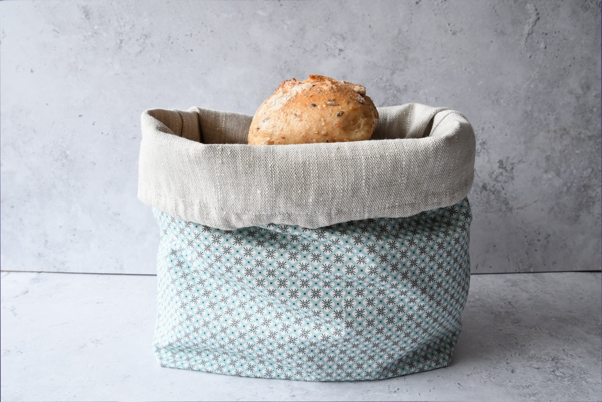 Brotbeutel "Primel" von Fabelhaftewerkstatt aus Baumwolle und Leinen, der umgeklappt als Brotkorb mit frischen Brötchen steht.