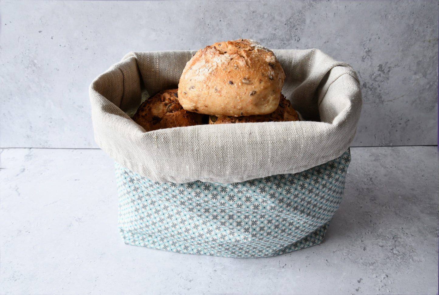 Brotbeutel "Primel" von Fabelhaftewerkstatt aus Baumwolle und Leinen, der umgeklappt als Brotkorb mit frischen Brötchen steht.