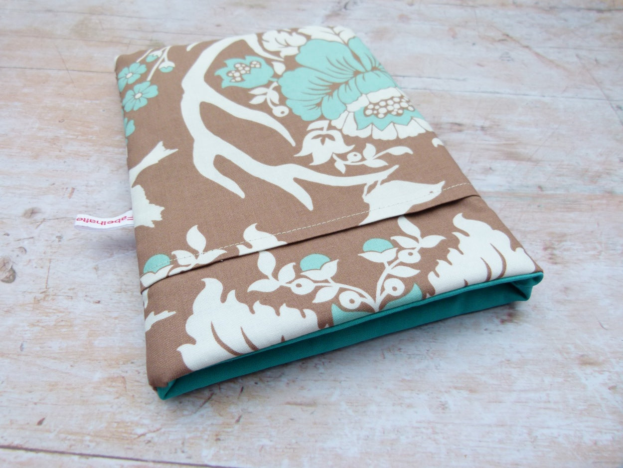 Handgefertigte, gepolsterte Buchtasche der Fabelhaften Werkstatt aus braunem Stoff mit einem detailreichen Natur-Motiv . Gut sichtbar ist das Innenfutter und das aufgesetzte Vorderfach für Zubehör auf der flach liegenden Hülle.