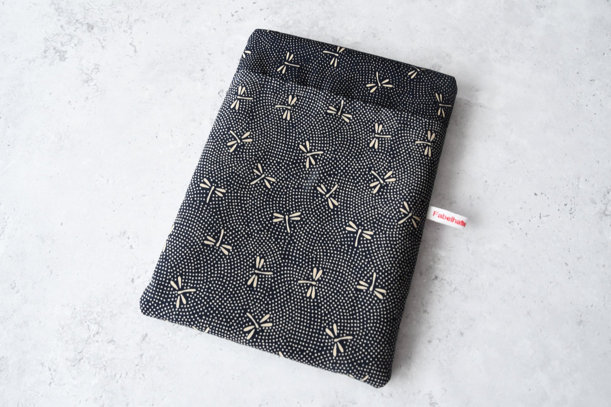 andgefertigte, gepolsterte Buchtasche der Fabelhaften Werkstatt aus dunkelblauem Stoff mit einem edlen japanischen Muster aus hellen Libellen. Das Produktfoto zeigt das flach liegende Design mit Fokus auf das praktische, aufgesetzte Vorderfach.
