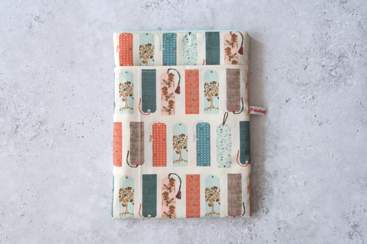Handgefertigte, gepolsterte Buchtasche der Fabelhaften Werkstatt aus hellem Stoff, bedruckt mit einem kreativen Muster aus vielen bunten, unterschiedlich gestalteten Lesezeichen. Das Produktfoto zeigt das flach liegende Design mit dem praktischen Vorderfach.