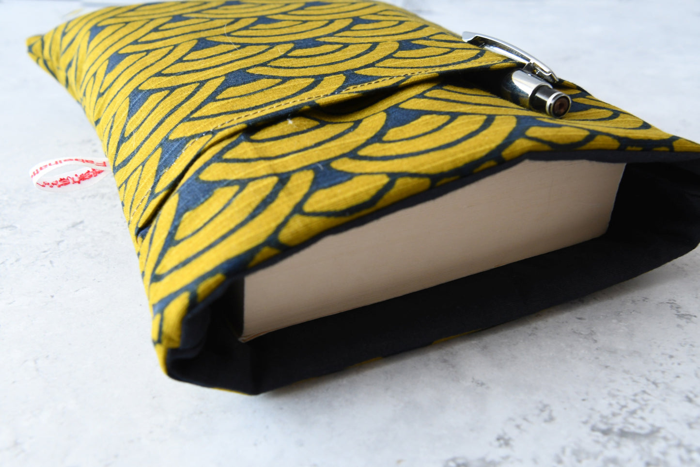 Elegante, dunkelblaue Buchtasche mit goldenem japanischen Wellenmuster in Benutzung. Ein dickes Taschenbuch schaut oben leicht aus der gepolsterten Hülle heraus. Im vorderen Fach steckt  ein Kugelschreiber.