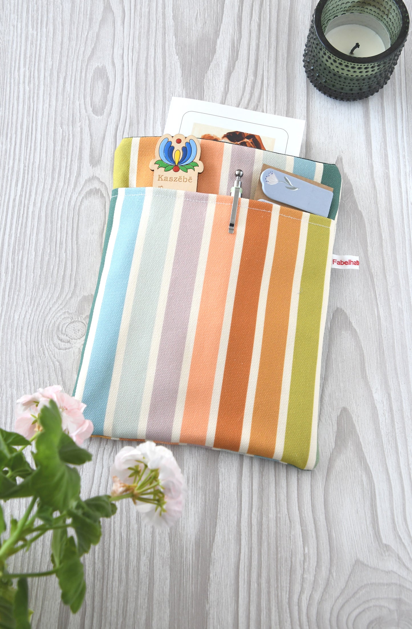 Gepolsterte Buchtasche aus Baumwolle mit bunten, pastellfarbenen Streifen, flach von oben fotografiert.
