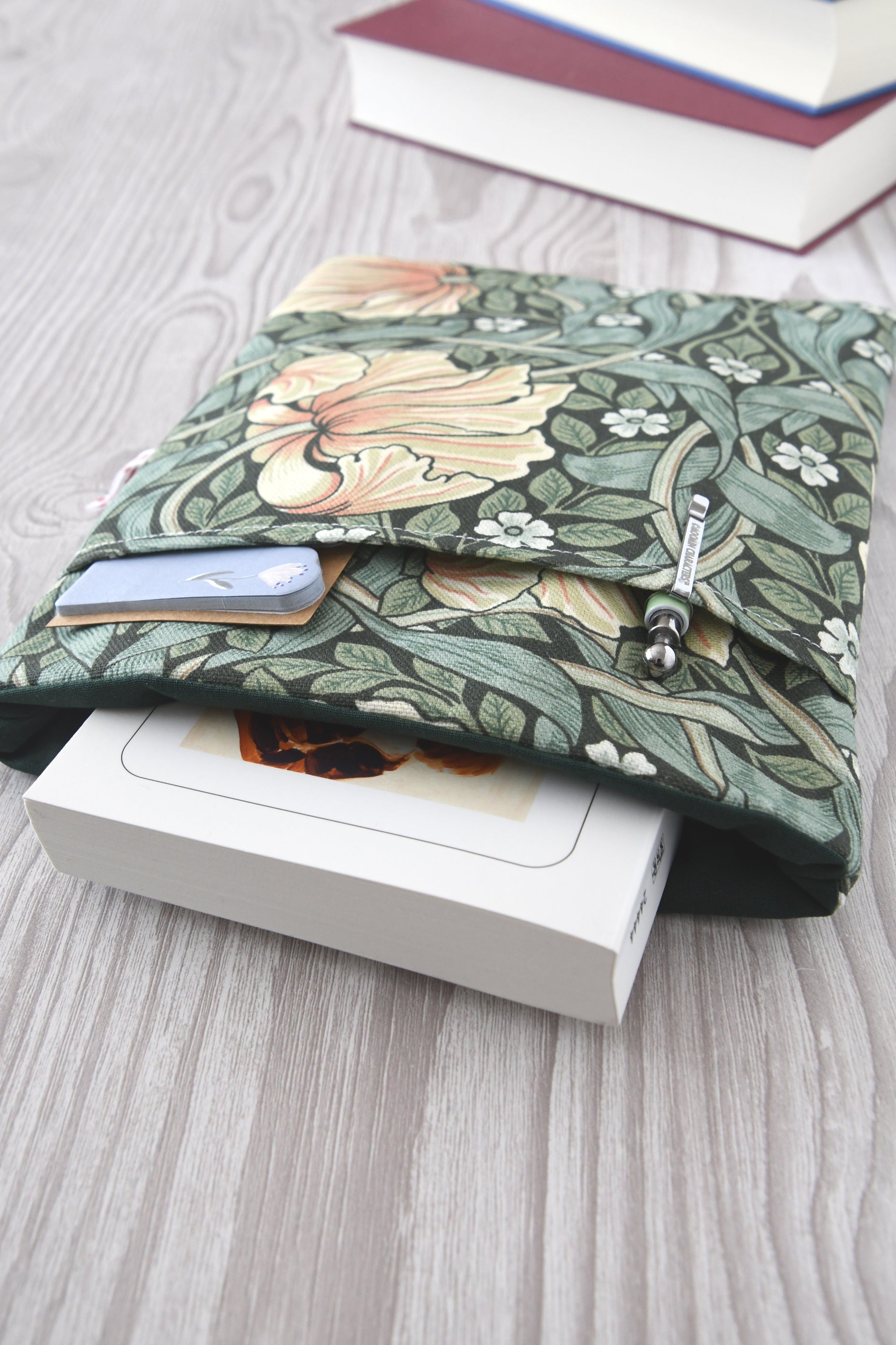 Draufsicht auf die geöffnete Buchtasche im William Morris Stil mit eingestecktem Buch sowie einem Stift und Lesezeichen in der Vordertasche.