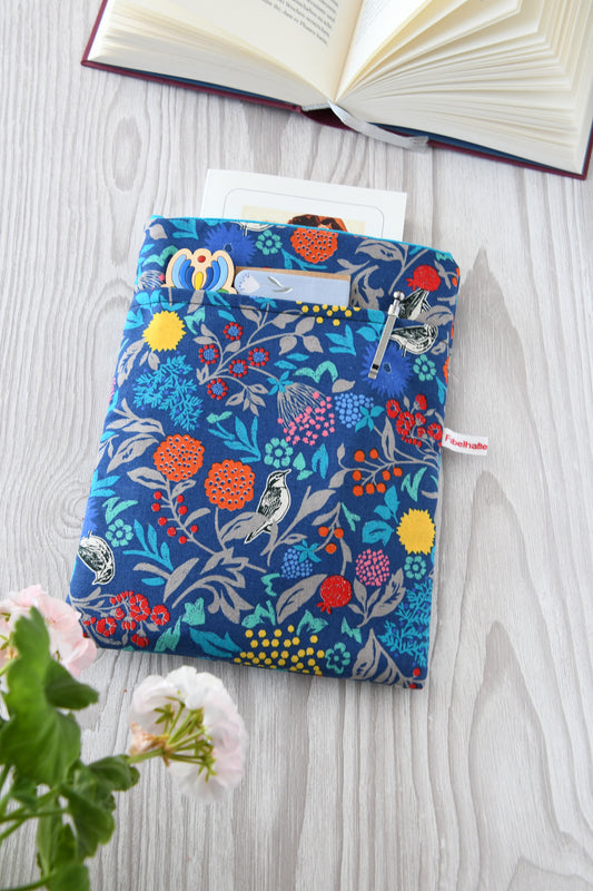 Handgefertigte, gepolsterte Buchtasche der Fabelhaften Werkstatt aus blauem Stoff, bedruckt mit einem eleganten Blumenmuster und kleinen Vögeln zwischen den Blüten. Das Foto zeigt das praktische, aufgesetzte Vorderfach auf der flach liegenden Hülle.