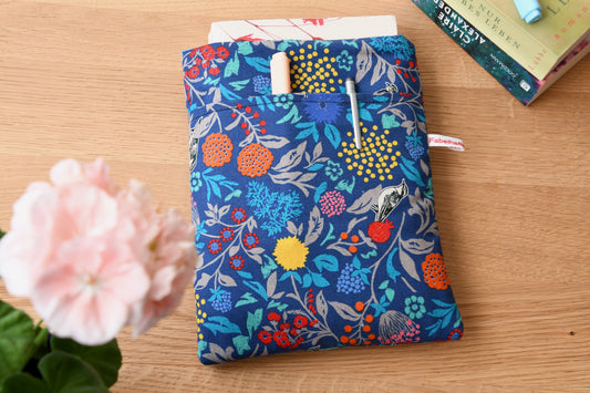 Handgefertigte, gepolsterte Buchtasche der Fabelhaften Werkstatt aus blauem Stoff, bedruckt mit einem eleganten Blumenmuster und kleinen Vögeln zwischen den Blüten. Das Foto zeigt das praktische, aufgesetzte Vorderfach auf der flach liegenden Hülle.