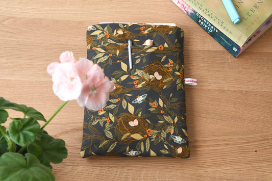 Handgefertigte, gepolsterte Buchtasche der Fabelhaften Werkstatt aus braunem Stoff mit einem detailreichen Natur-Motiv aus kleinen Vogelnestern und hellen Vogeleiern. Gut sichtbar ist das aufgesetzte Vorderfach für Zubehör auf der flach liegenden Hülle.