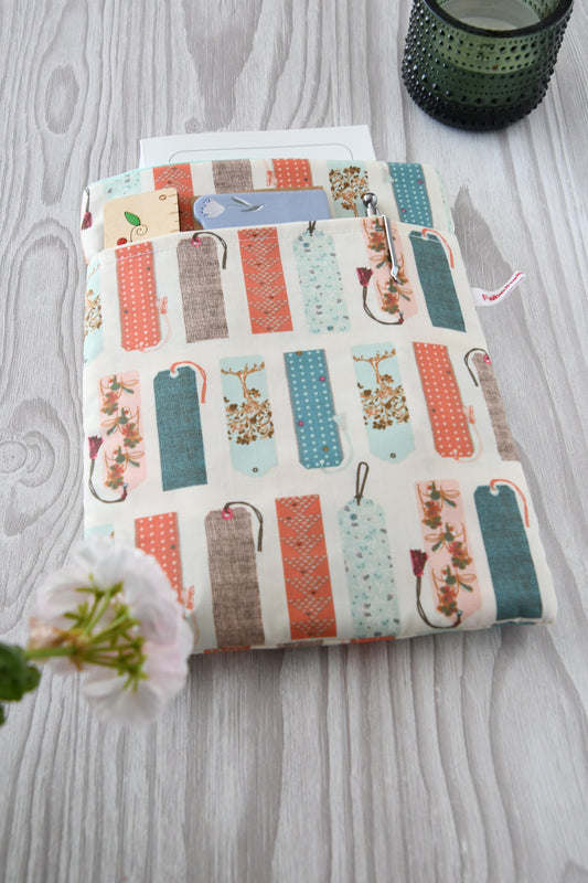 Handgefertigte, gepolsterte Buchtasche der Fabelhaften Werkstatt aus hellem Stoff, bedruckt mit einem kreativen Muster aus vielen bunten, unterschiedlich gestalteten Lesezeichen. Das Produktfoto zeigt das flach liegende Design mit dem praktischen Vorderfach.
