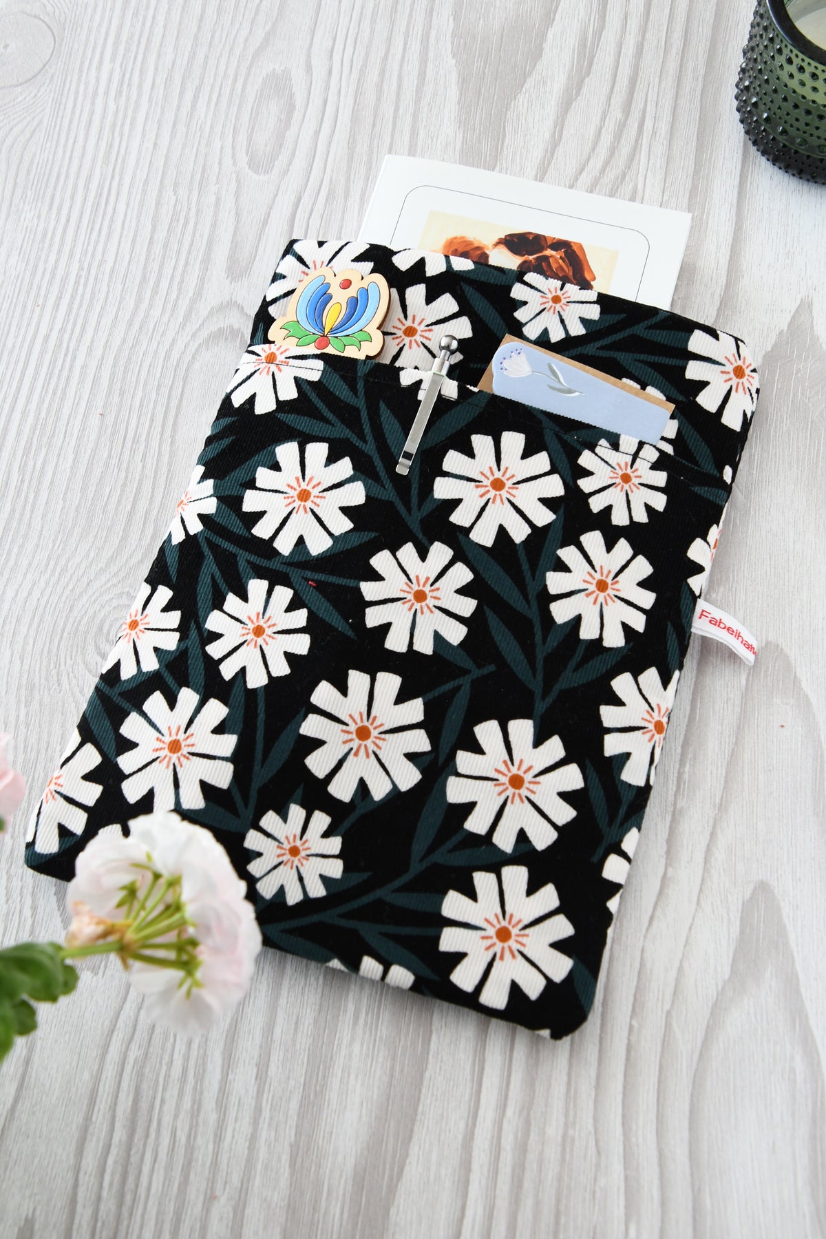 Fröhliche, weich gepolsterte Buchtasche mit einem sommerlichen Margeriten-Muster (weiße Blüten mit orangenfarbender Mitte).  Im cleveren Vorderfach sind Stifte und kleine Haftnotizen griffbereit platziert.