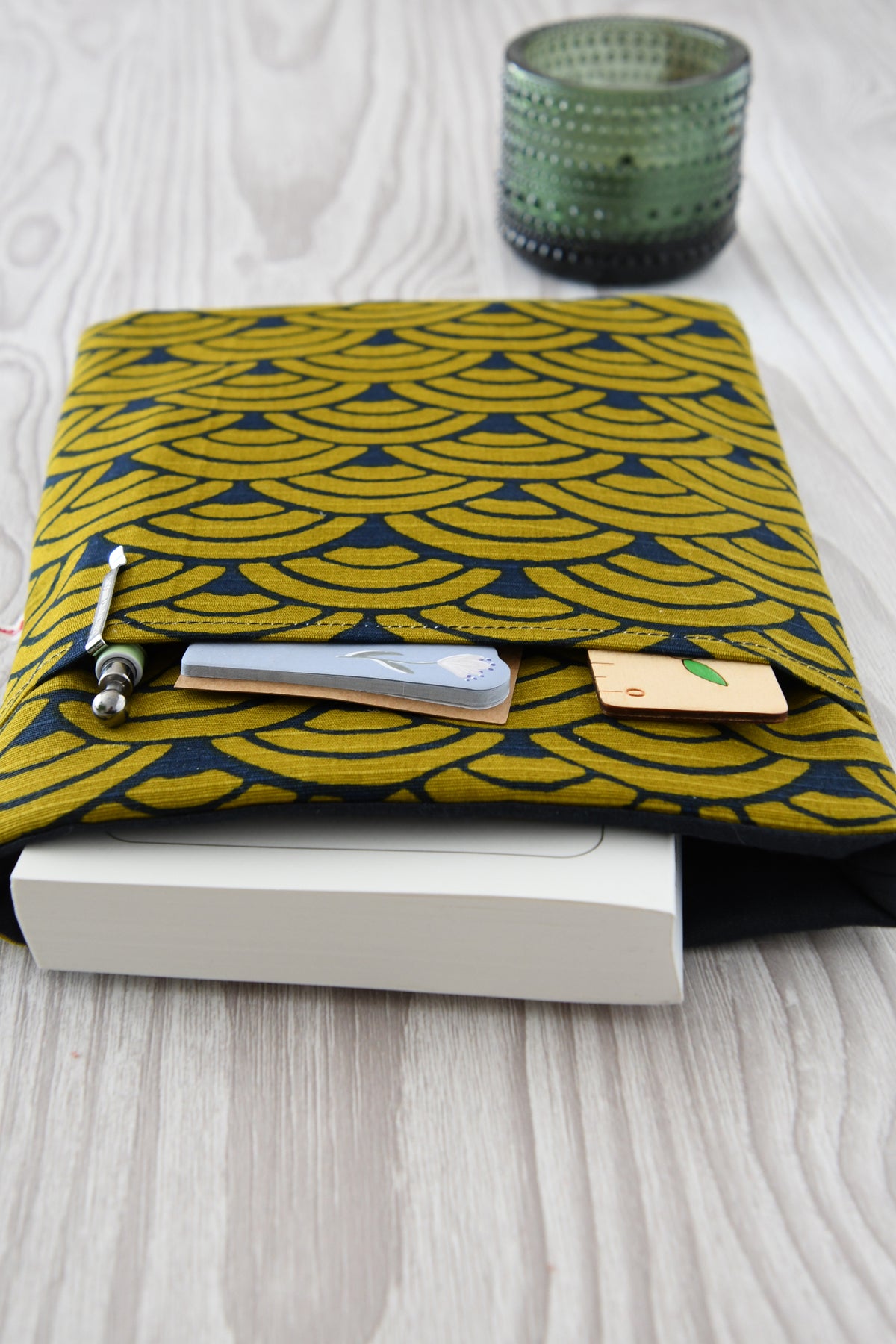 Elegante, dunkelblaue Buchtasche mit goldenem japanischen Wellenmuster in Benutzung. Ein dickes Taschenbuch schaut oben leicht aus der gepolsterten Hülle heraus. Im vorderen Fach steckt  ein Kugelschreiber.