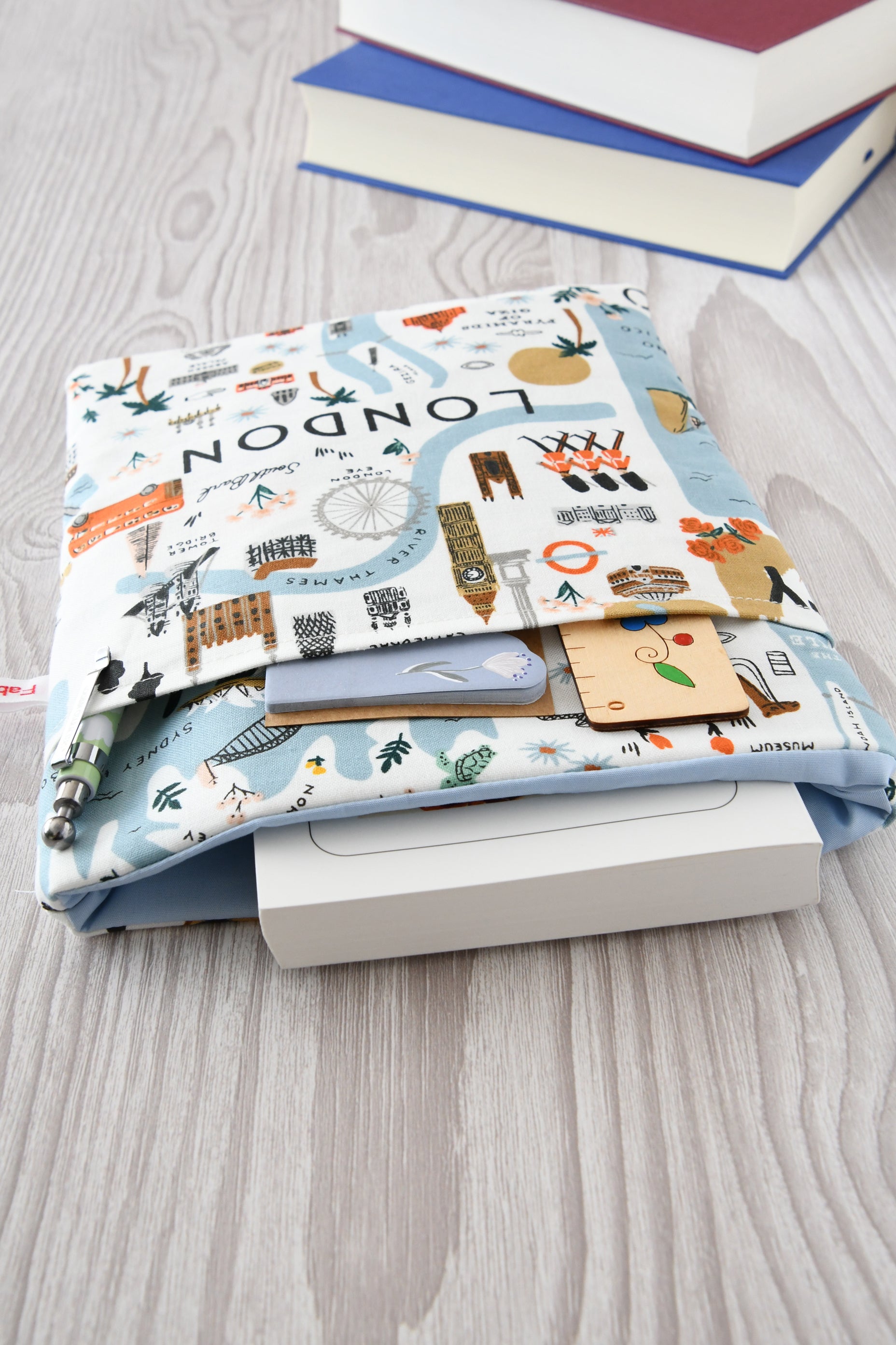 Draufsicht auf die geöffnete Buchtasche Citytrip mit eingestecktem Buch sowie Stift und Lesezeichen in der praktischen Vordertasche.