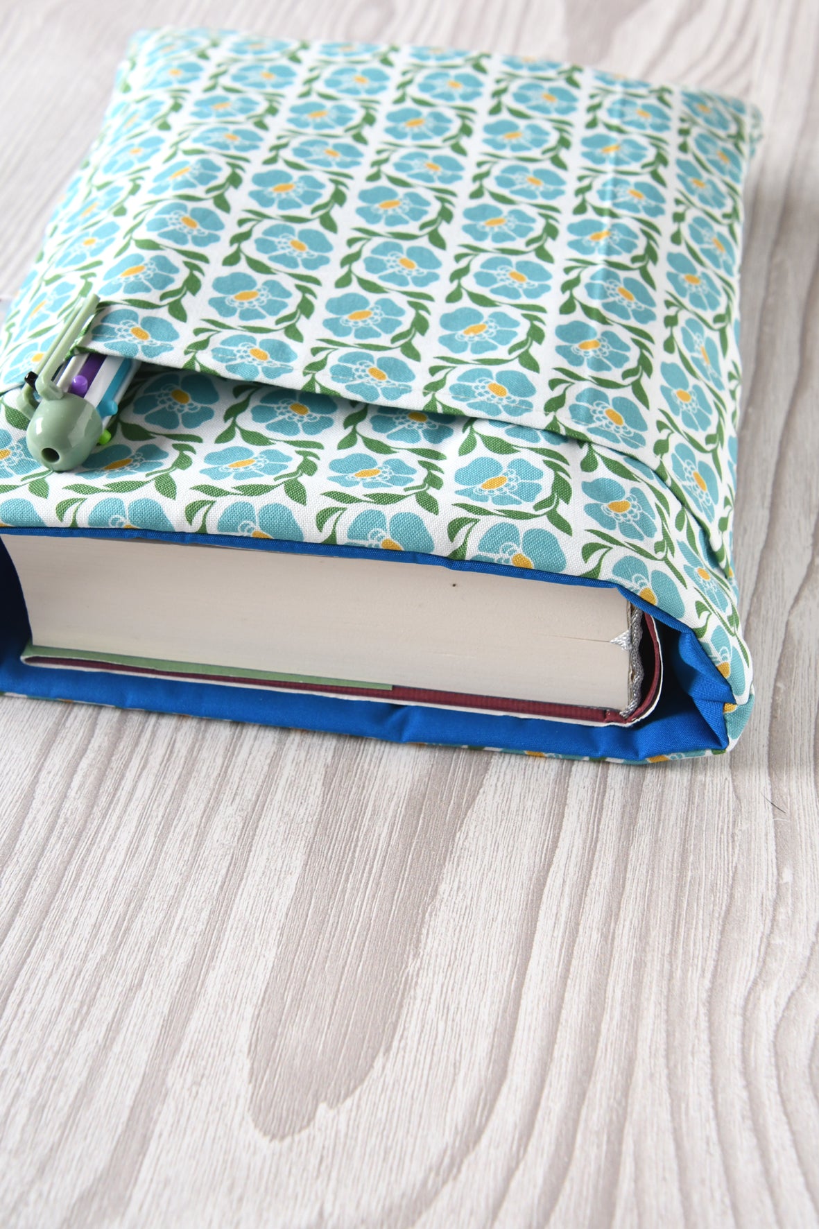 Große Buchtasche "Franziska" in Größe L mit blauem Blumenmuster. Ein dicker Hardcover-Wälzer mit ca. 500 Seiten ist passgenau in die Stoffhülle eingesteckt.