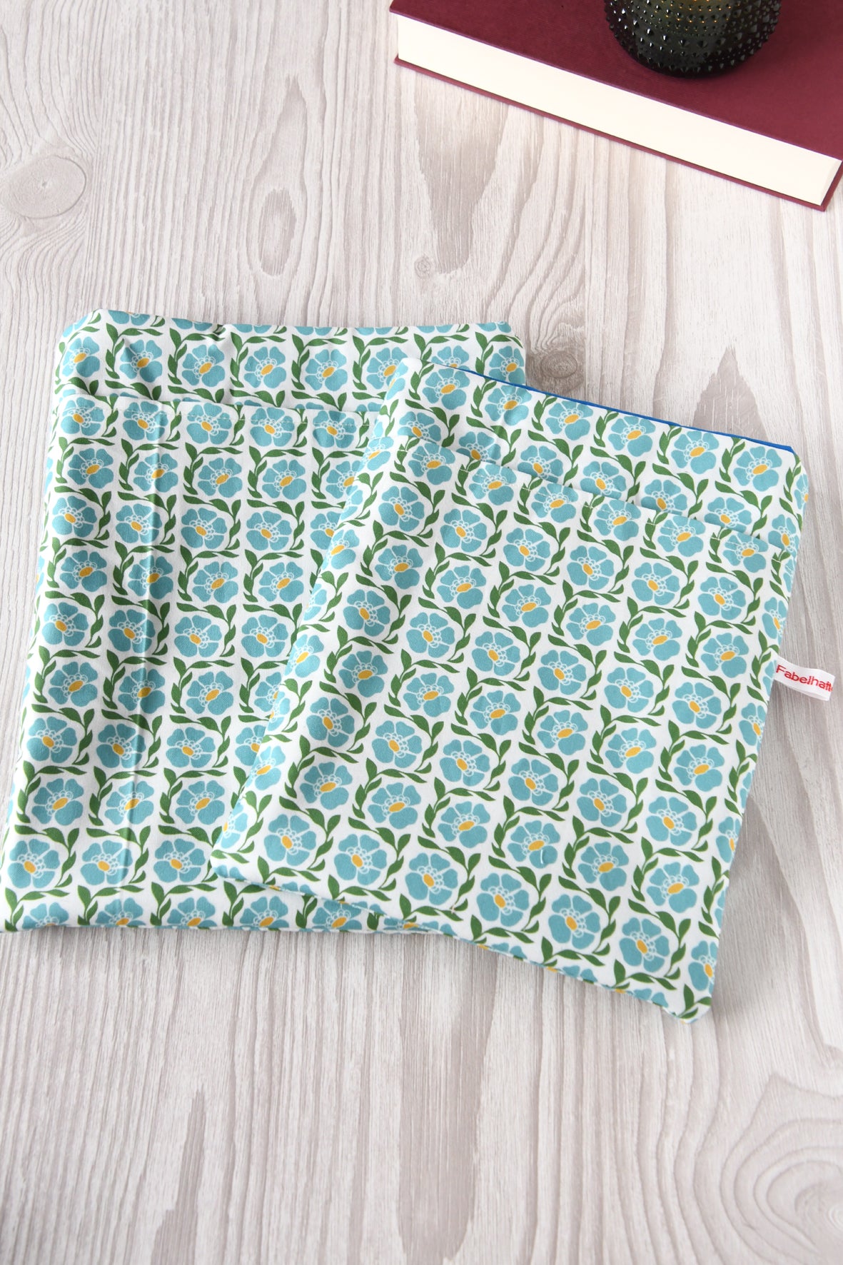Größenvergleich der Buchtasche "Franziska" im blauen Blumenmuster: Links die große Buchtasche L für Hardcover-Bücher und Tablets, rechts die Standardgröße M für Taschenbücher, nebeneinander auf einem hellen Hintergrund.
