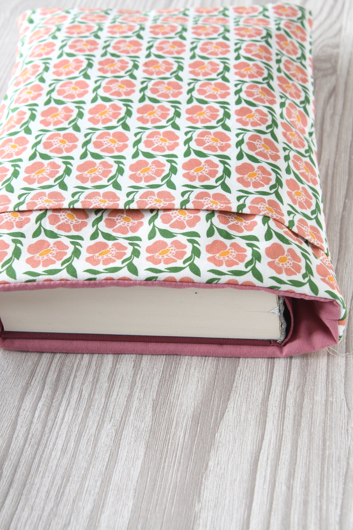 Große Buchtasche "Fanny" in Größe L mit rosafarbendem Blumenmuster. Ein dicker Hardcover-Wälzer mit ca. 500 Seiten ist passgenau in die Stoffhülle eingesteckt.